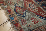 Antique Anatolian rug, tattered edge exposing foundation, with red, blue, apricot patterns.