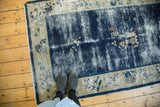 Antique Peking rug with worn cobalt blue pictorial field and ivory border displaying floral motifs.