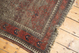 Tattered fringe and worn edge of a vintage Belouch rug, with geometric brown and blush patterns.