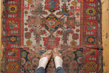 Antique Malayer rug detail: vibrant red geometric border, stylized motifs on ivory field, frayed side.
