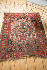 Antique Malayer rug corner showcasing red and blue Herati floral patterns, tattered edge, and visible foundation.