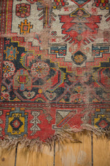 Antique Malayer rug detail showing worn floral patterns, bright red border, and frayed edge.