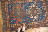 Vintage Caucasian rug detail: indigo geometric starburst medallion, floral border, and tattered fringe.