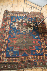 Charcoal starburst and madder red motifs on indigo vintage Caucasian rug with visible foundation.