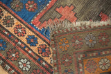 Tattered end of vintage Caucasian rug showing foundation and geometric indigo, orange, red pile.