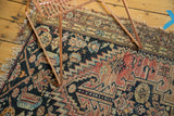 Faded geometric motifs, tattered edge, and noticeable hole in the dark field of the antique Malayer rug.