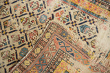 Folded corner of antique Shirvan rug, showing Marsali geometric lattice, tattered fringe, and visible foundation.