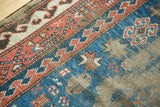 Antique Caucasian rug detail: rust, indigo, and ivory geometric borders with wave motif and holed area.