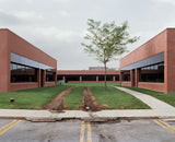 Joe Farrell's Schoolyard color photograph of symmetrical brick buildings with a central tree and muddy tire tracks.