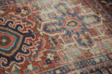 Karaja rug's worn pile revealing foundation, geometric serrated leaves in brick red, navy.