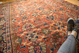 Close-up of vintage Mahalati rug, rich terra cotta, palmette and lotus motifs, visible even wear, with feet.