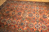 Repeating palmette and lotus flower motifs on a terra cotta Mahalati rug with even wear.