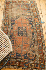 Indigo and terra cotta geometric starbursts on antique Kurdish rug, with visible foundation and fraying.