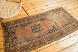 Detail of antique Kurdish runner showing coffee brown and indigo field with starburst motifs, tatter, and exposed foundation.