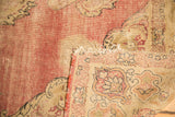 Folded corner of antique Kerman rug showing tattered fringe, visible foundation, and faded floral motifs.