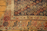 Antique Kurdish Hamadan rug corner with tattered edge and worn indigo field, showing tribal motifs.