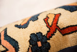 Hand-knotted pile of rug fragment pillow with beige, navy, red-orange, and peach curvilinear motifs.
