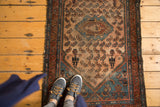 Vintage Malayer rug's dusty rose field, herati leaves, and corner man motif, with visible wear.