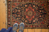 Vintage Hamadan rug corner, navy field, brick red border, floral cross sections, and tattered fringe.
