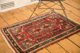 Corner view of vintage Hamadan rug with cherry red field, floral pattern, and tattered fringe.