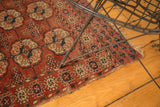 Antique Turkmen rug corner shows geometric gul motifs in navy, ivory, and peach with a tattered edge.