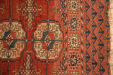 Antique Turkmen rug: repeating gul motifs, dark red, navy, peach, ivory, and tattered fringe.