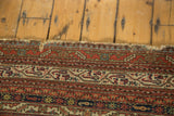 End of a hand-knotted antique Malayer rug, showing light tatter and geometric patterns in brick red, blue, and ivory.