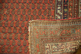 Antique Malayer rug pile with repeating pale cinnabar red boteh, folded to reveal hand-knotted foundation.