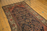 Antique Malayer rug showing worn edges, etched pile, and intricate navy, blush floral patterns.