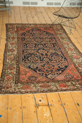 Detailed lower section of an antique Malayer rug, showing ornate navy field vinery and blush floral border with light tatter.