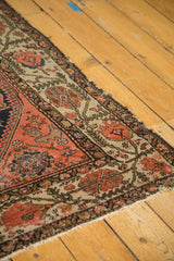Antique Malayer rug's corner with worn coral field, traditional floral border, tattered edge.