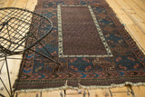 Antique Belouch rug corner with aubergine field, indigo wave border, tattered ends.