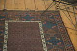 Aubergine field motifs, ivory geometric border, indigo wave pattern, and worn pile of antique Belouch rug.