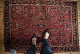 Corner of vintage Sarouk rug showing tattered side, burgundy field, and navy border.