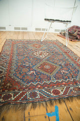 A low angle view displaying the full geometric pattern and triple diamond medallions of an antique Qashqai rug.