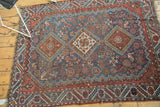 Angled view of an antique Qashqai rug highlighting the geometric border and evenly worn pile.