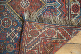 Folded corner of an antique Qashqai rug revealing its hand-knotted back and original wool fringe.