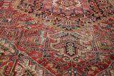 Vintage Heriz carpet's intricate brick red field with blue and green motifs, showing foundation wear.