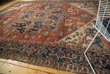 Antique Serapi carpet's navy border, geometric tendrils, brick red field, and tattered selvage.