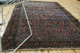 Antique American Sarouk rug showcasing intricate elongated floral motifs, a dark dusty rose field, and tattered fringe.