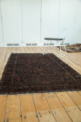 Antique American Sarouk rug's tattered end, showing dark cochineal field and floral motifs.