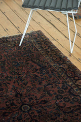 Antique Sarouk rug corner with detailed navy floral motifs on a dusty rose field, low pile.