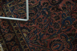Intricate elongated floral and vine patterns on an antique Sarouk rug in dusty rose, navy, and gold.