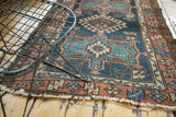 Antique Karaja rug's diamond medallion, dark denim blue field, pale terra cotta border, and tattered fringe.