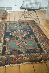 Antique Karaja rug's geometric patterns in dark blue, terra cotta, green, showing tattered end.