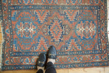 Antique Heriz rug left edge, showing brick red, blue geometric motifs, and tattered fringe.