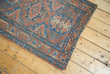Antique Heriz rug corner: intricate geometric border, brick red, ocean blue, ivory, and frayed edges.