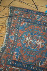 Tattered fringe and intricate blue, brick red, and ivory geometric pattern on an antique Heriz rug.