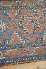 Brick red and blue geometric patterns with visible wear and tattered edge on the Antique Heriz rug.