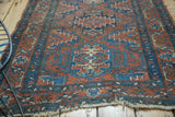 Tattered fringe and geometric patterns in brick red and blue on an antique Heriz rug.
